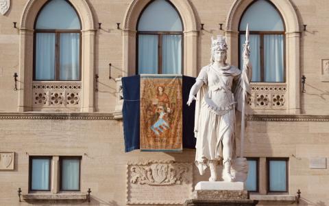 Statua e bandiera su edificio storico con finestre ad arco.